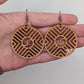 Image of a pair of Circle earrings with a Geometric Chevron design on a hand showing the size against a white background, they are three finger widths in length and three wide. They are Cherry Wood and have black fixings.