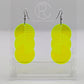 A pair of large acrylic earrings with black ear wire hook fixings. Each earring is 3 circles overlapping and entwined with  engraved line decorations. The colour is neon Green and they are hung on a clear stand against a white background.