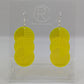 A pair of large acrylic earrings with silver ear wire hook fixings. Each earring is 3 circles overlapping and entwined with  engraved line decorations. The colour is neon yellow and they are hung on a clear stand against a white background.