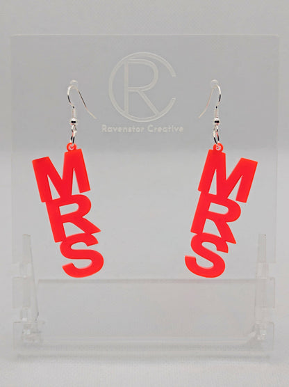 A pair of earrings with Silver ear wire hook fixings. Each one is the word Mrs in capital letters. They are Neon Pink in colour. These are ideal for a Hen do or Bachelorette Party. They are on clear stands against a white background.