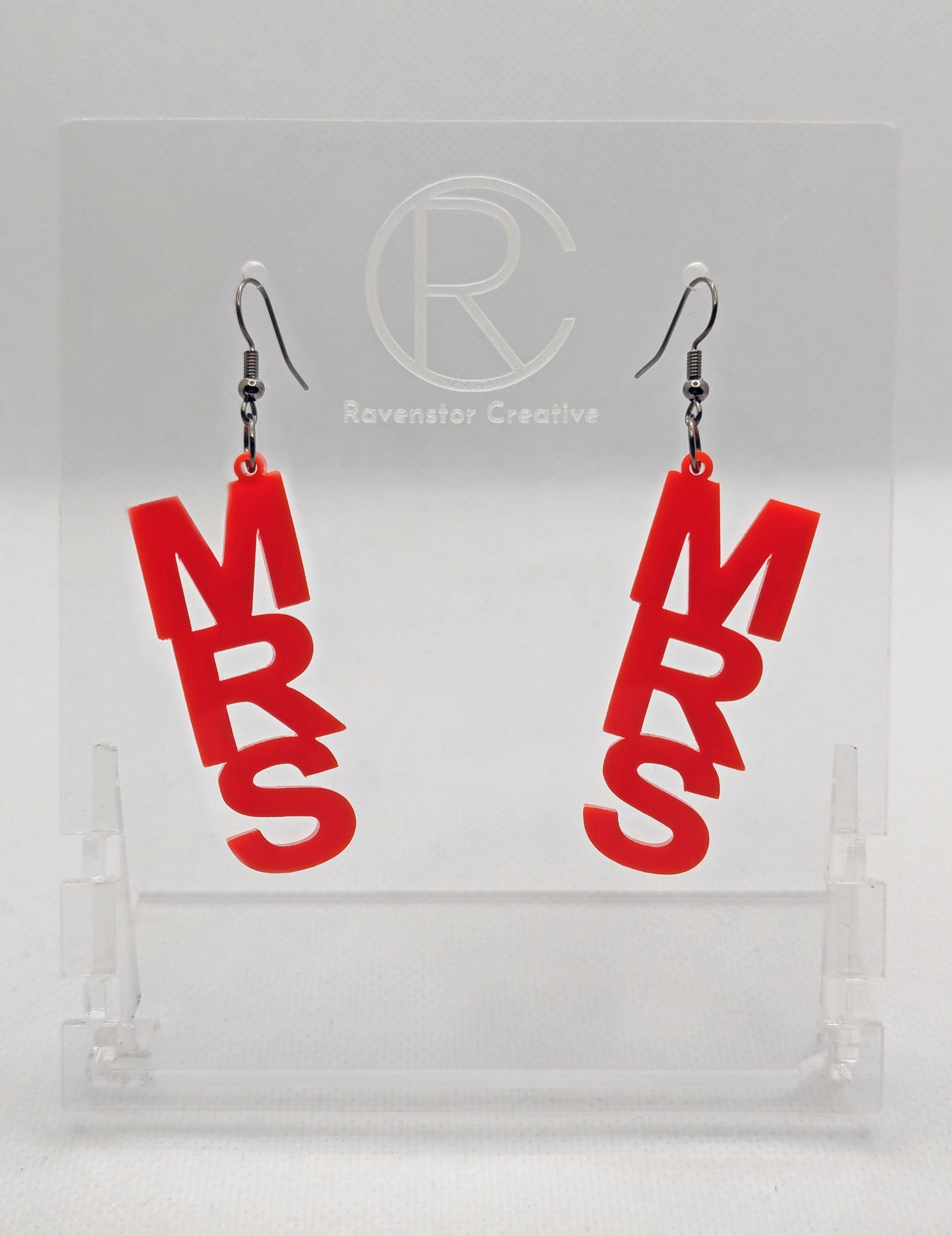 A pair of earrings with Black ear wire hook fixings. Each one is the word Mrs in capital letters. They are Red in colour. These are ideal for a Hen do or Bachelorette Party. They are on clear stands against a white background.