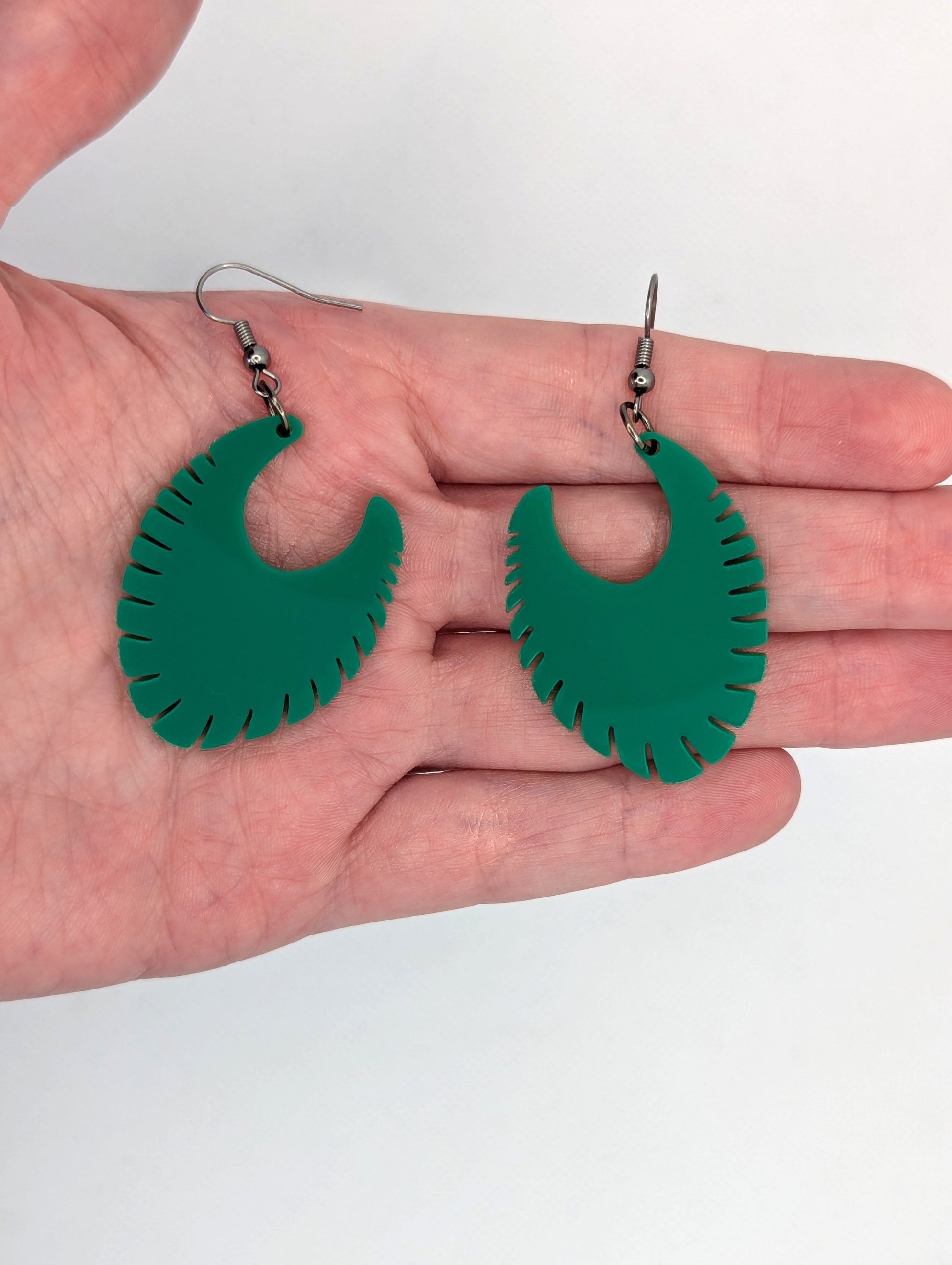 Image of a pair of acrylic earrings with black ear wire hook fixings. They are Ribbed half moon shapes with ridges around one side. They are against a hand to show the size of two and a half finger widths long and two wide.