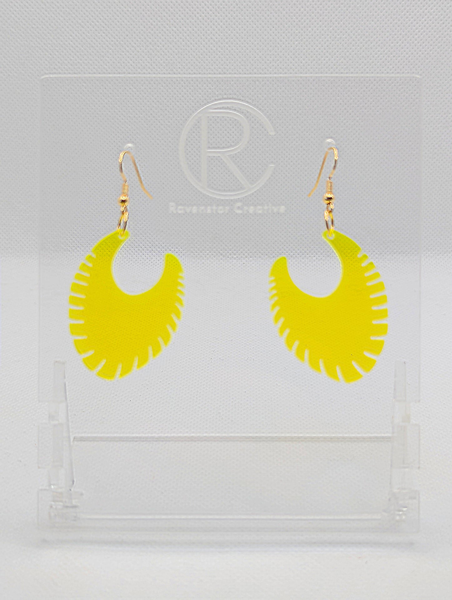 Image of a pair of acrylic earrings with Gold ear wire hook fixings. They are Ribbed half moon shapes with ridges around one side. They are Neon Orange and are on clear stands with the Ravenstor Creative logo on them against a white background.