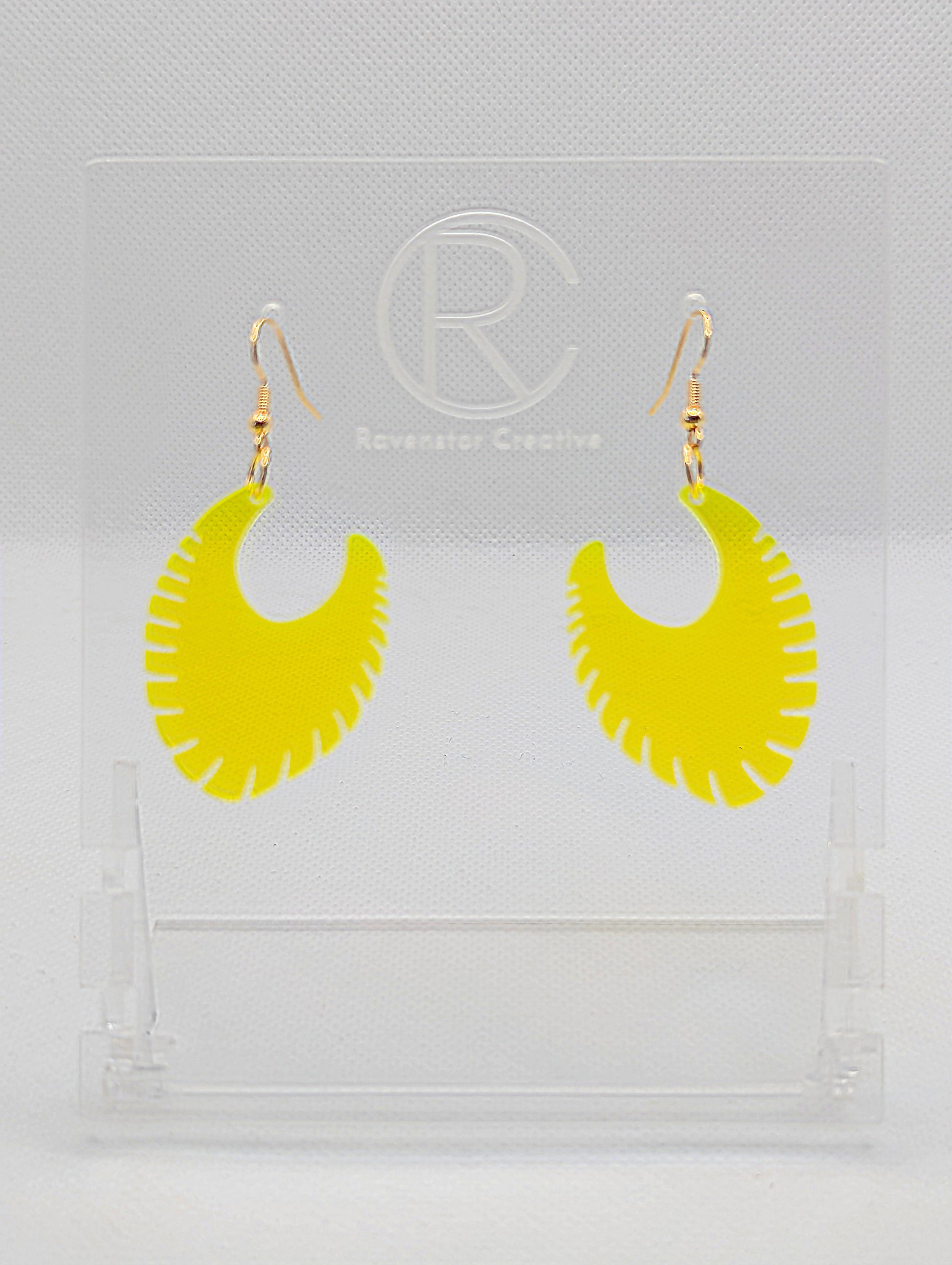 Image of a pair of acrylic earrings with Gold ear wire hook fixings. They are Ribbed half moon shapes with ridges around one side. They are Neon Orange and are on clear stands with the Ravenstor Creative logo on them against a white background.