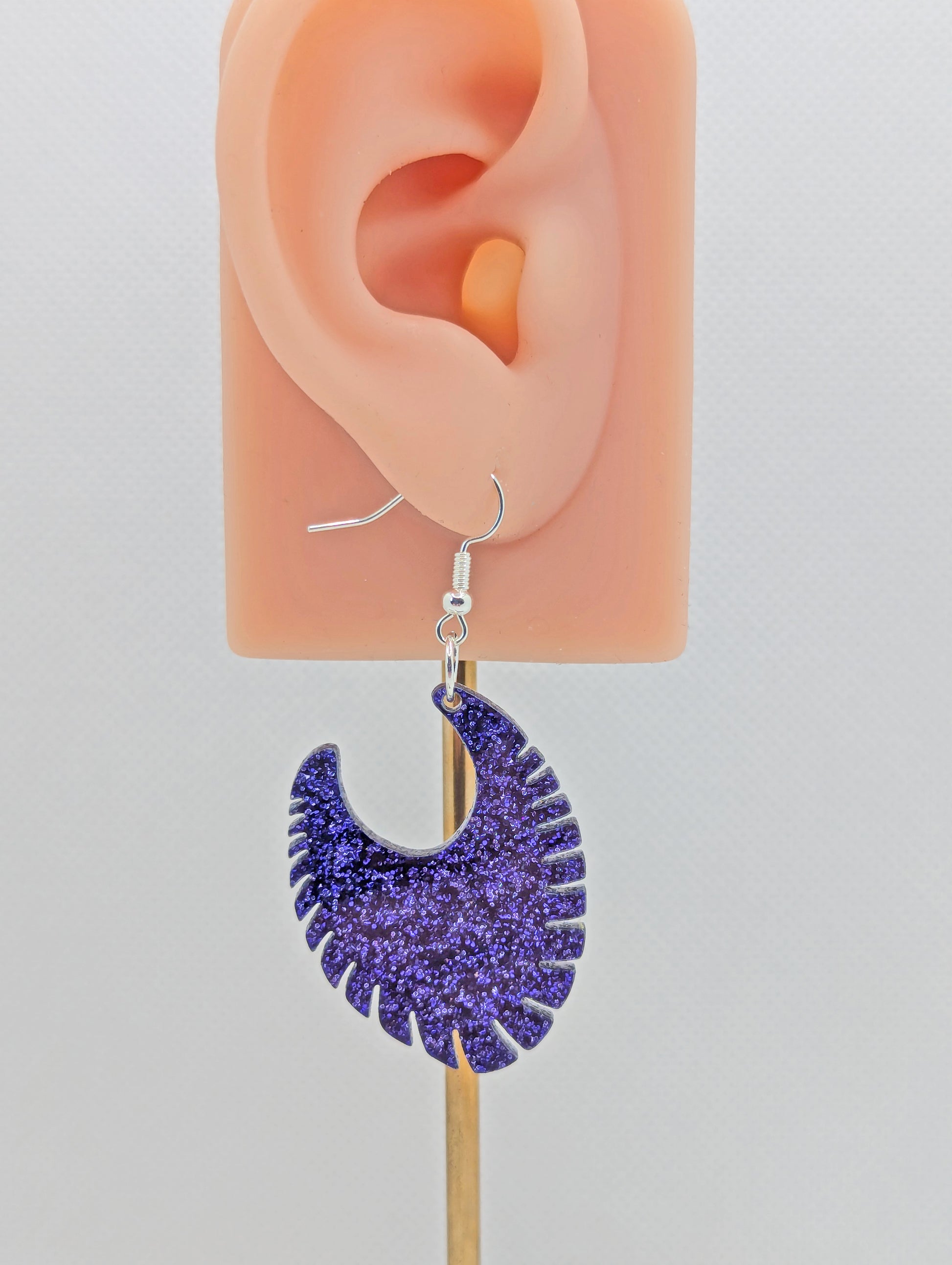 Image of an acrylic earring with a Silver ear wire hook fixing. It is a Ribbed half moon shape with ridges around one side. It is Purple Glitter and is on an ear to show the size against a white background.