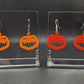 Shows 2 pairs of earrings with ear wire hook fixings. They are scary Halloween pumpkin shapes. The colours of them are Orange and Red. They are on see through stands with the Ravenstor Creative logo on them against a dark background.