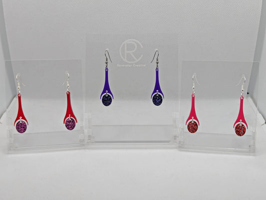 Shows three pairs of 2 part earrings with ear wire hook fixings. They are slim teardrop shapes. The colours are Red top and Pink glitter oval, Purple top and Purple Glitter oval, Hot pink top and Red glitter oval.