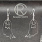 Shows a pair of earrings with silver ear wire hook fixings. They are spooky moaning ghost shapes. The colour of them is clear/see through. They are on a see through stand that has the Ravenstor Creative Logo and its against a dark background.