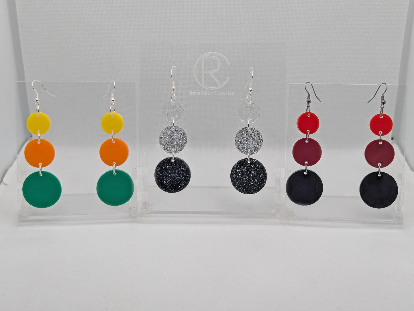 Three pairs of earrings, each has three circles dangling from each other, the top is the smallest and they get bigger as they go down. Colours are (from the top) yellow, orange and green. Glitters Clear, Silver and Black. Red, Maroon and Black.