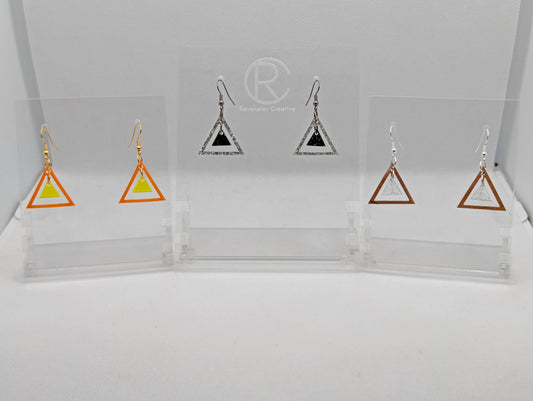 Shows three pairs earrings ear wire hook fixings. They are Triangle shapes with a smaller Triangle dangling inside them. The colours are orange outer with neon Yellow, Silver Glitter outer, Black & Silver inner and cherry wood outer and Clear sparkle