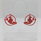 A pair of acrylic earrings with silver Ear wire hook fixings on a white background, they are a circle with a scene cut out of a witch on her broom with a cat perched on the broom. The colour is a lovely Red Glitter.