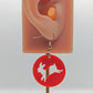 An acrylic earring that has rose gold ear wire hook fixings against an ear to show the size. It is a Circle with an Easter bunny / Rabbit hopping cut out of it. It is Red in colour.