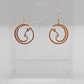 Shows a pair of earrings that have rose gold ear wire hook fixings. They are Full Moon inspired Cat shapes. They are in Cherry Wood and are against a white background on see through stand with the Ravenstor Creative logo on it.