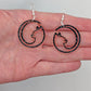 Image of a pair of earrings that are full moon inspired cat shapes, on a hand showing the size against a white background, they are 2 finger widths length the same again wide. They are black and silver glitter and have silver fixings.