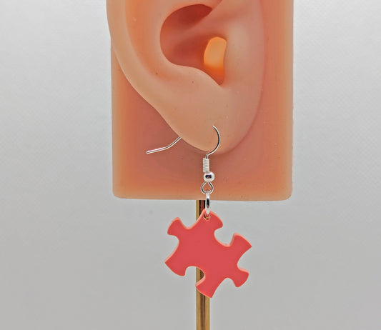 Shows an acrylic earring with silver ear wire hook fixings. It is a Jigsaw Game Piece Shape. The colour is Orange. It is on an ear showing the size against a white background.