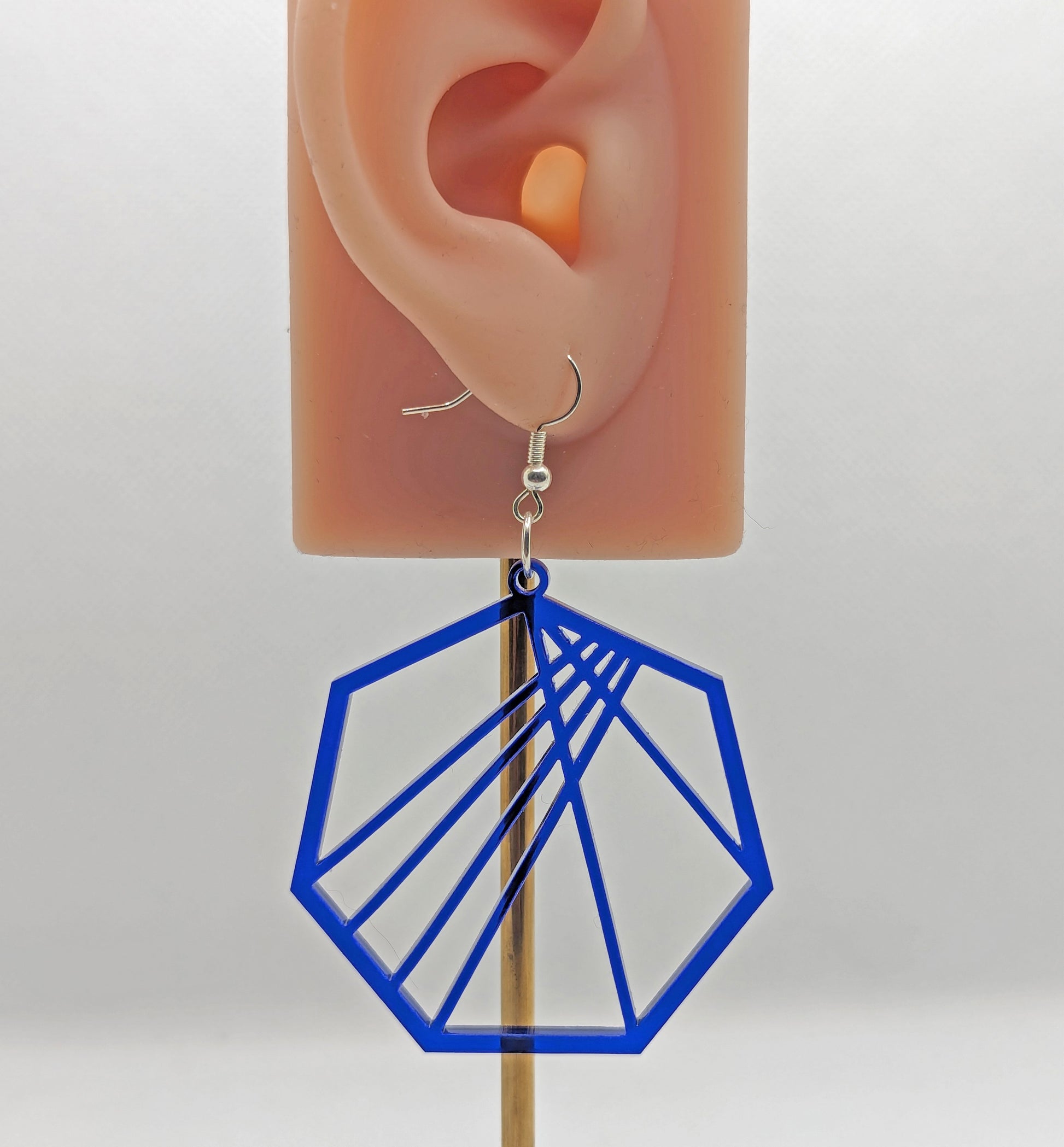 Image of a Geometric Heptagon earring on an ear showing the size against a white background. It is made from translucent blue acrylic and have silver fixings.