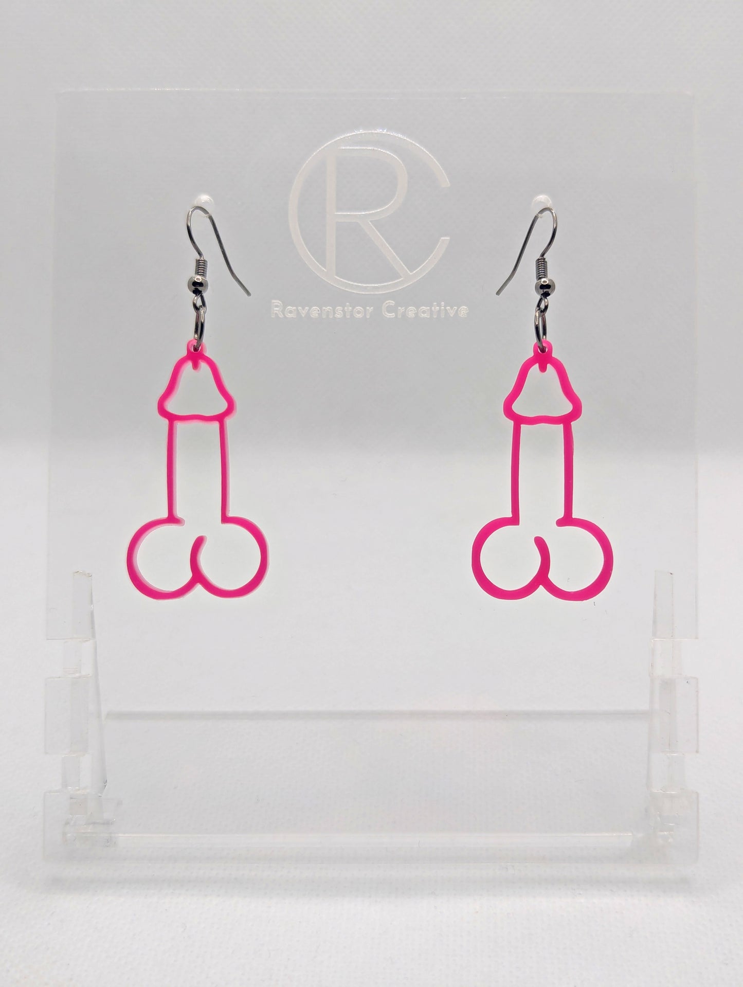 Image of a pair of earrings shaped like a Penis and Balls with Black wire hook fixings. These are ideal for funny Hen Dos or Bachelorette parties. The colour is Hot Pink and they are on clear stands against a white background.