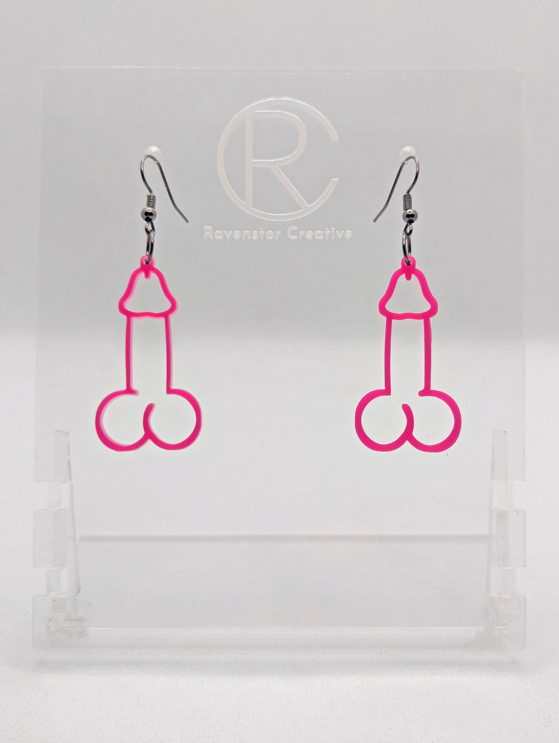 Image of a pair of earrings shaped like a Penis and Balls with Black wire hook fixings. These are ideal for funny Hen Dos or Bachelorette parties. The colour is Hot Pink and they are on clear stands against a white background.