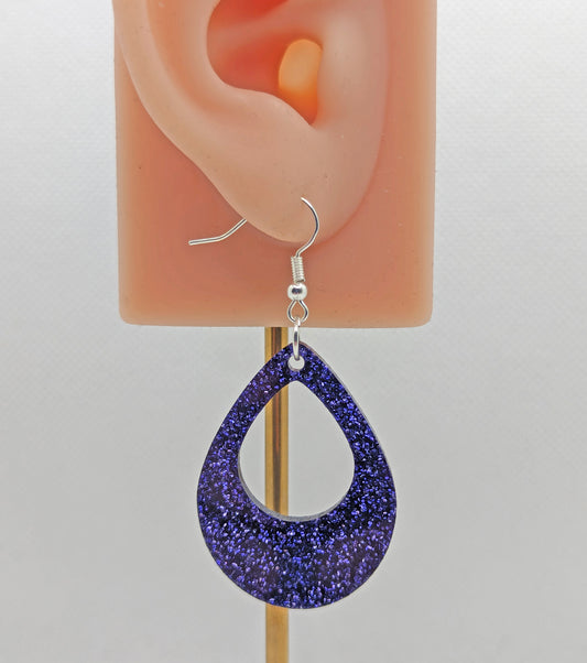 Image of a Teardrop shaped Hoop earring on an ear showing the size against a white background. It is made from purple glitter acrylic and have silver ear wire hook fixings.