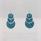 An image of snowman earrings with silver ear wire hook fixings. They are in three parts that dangle. They are made from Ice Blue glitter acrylic and are on a clear stand with the ravenstor creative logo on it against a white background