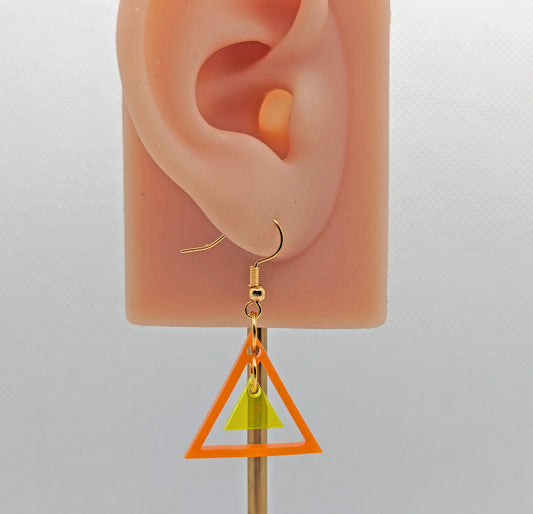 A triangle shaped earring with a smaller triangle dangling inside on an ear showing thier size. They are orange for the outer and neon yellow Glitter for the small inner. They have gold ear wire hook fixings.