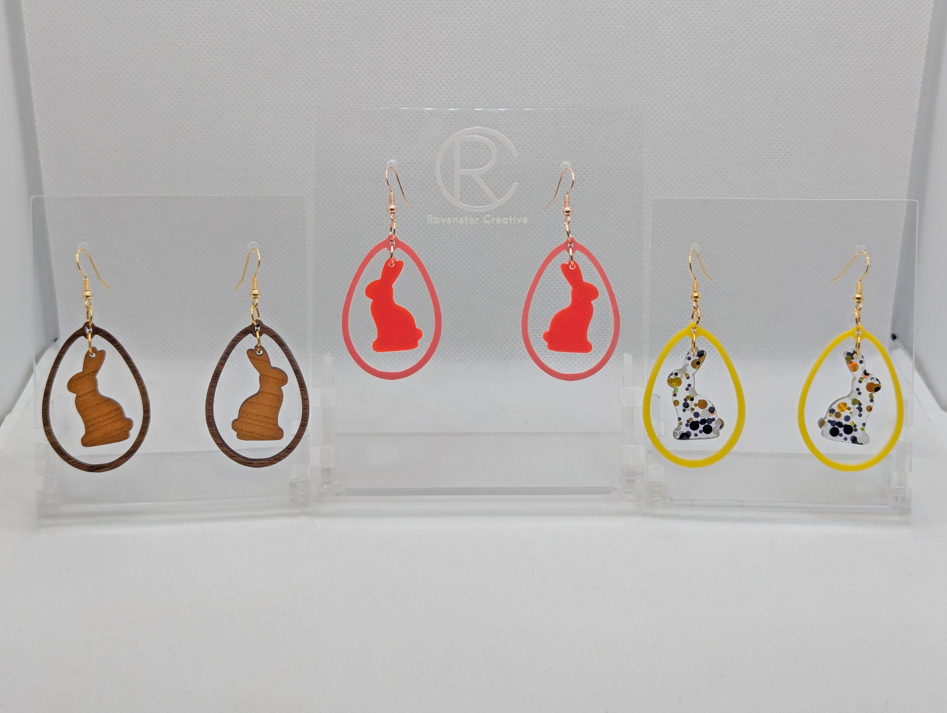 Three pairs of two part drop earrings with ear wire hook fixings. They are an egg shaped frame with a Bunny Rabbit dangling inside. The colours are Cherry Wood Bunny and Walnut Wood Egg, Neon Pink Bunny Sherbet Pink Egg, Lollipop Glitter and Yellow.