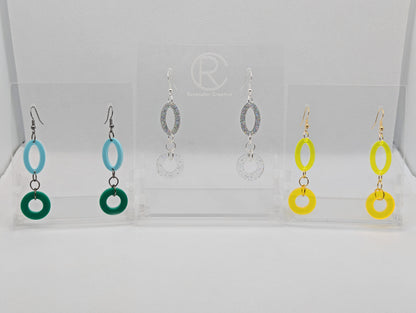 Three pairs of two part drop earrings with ear wire hook fixings. They are an oval with a circle dangling underneath joined by three jump rings. The colours are Spearmint and Green, Holographic Glitter and Clear sparkle, Neon Yellow and Neon Orange.