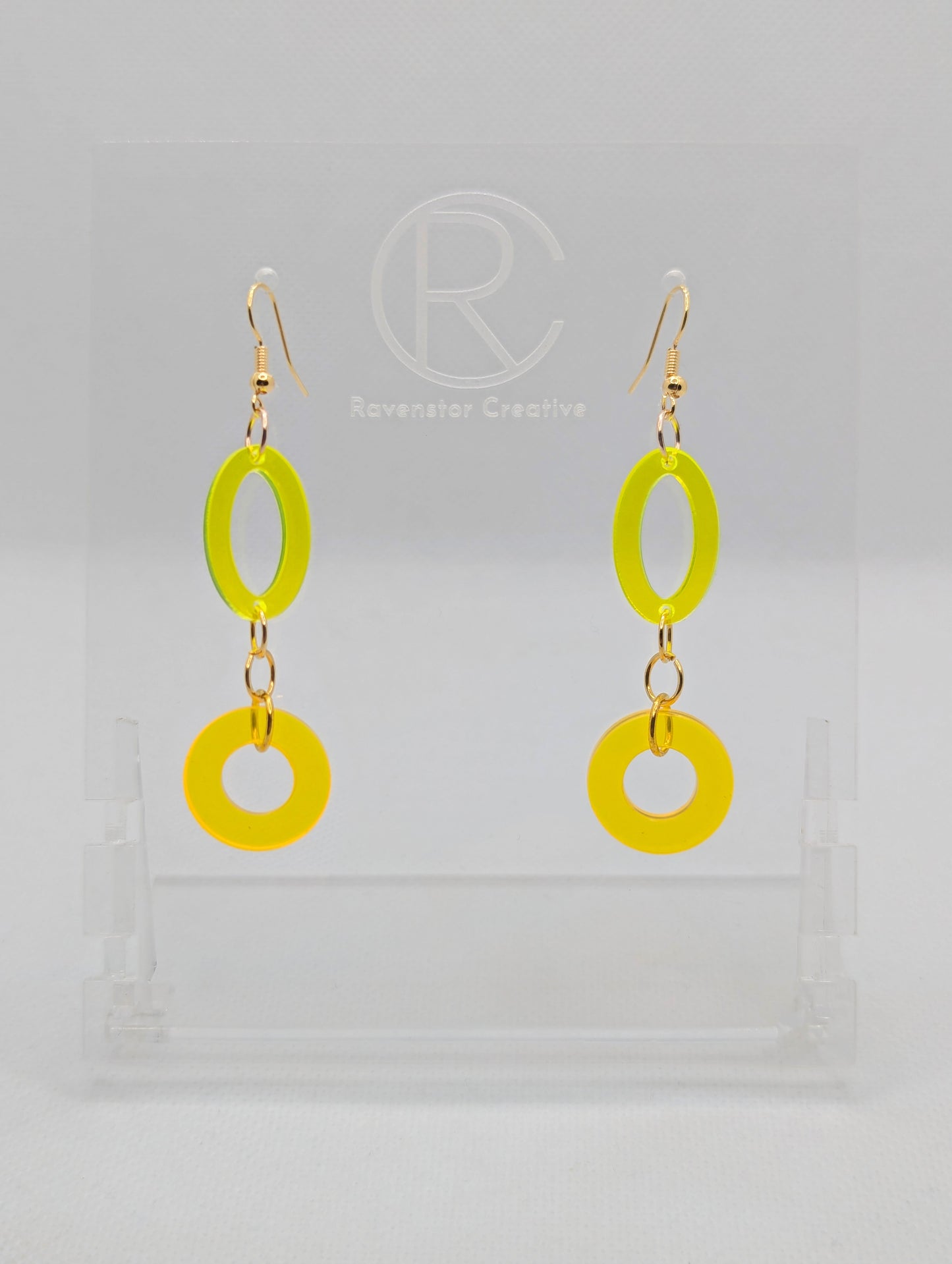 A pair of two part drop earrings with Gold ear wire hook fixings. They are an oval with a circle dangling underneath joined by three Gold jump rings. The colours are Neon Yellow for the oval and Neon Orange for the circle.