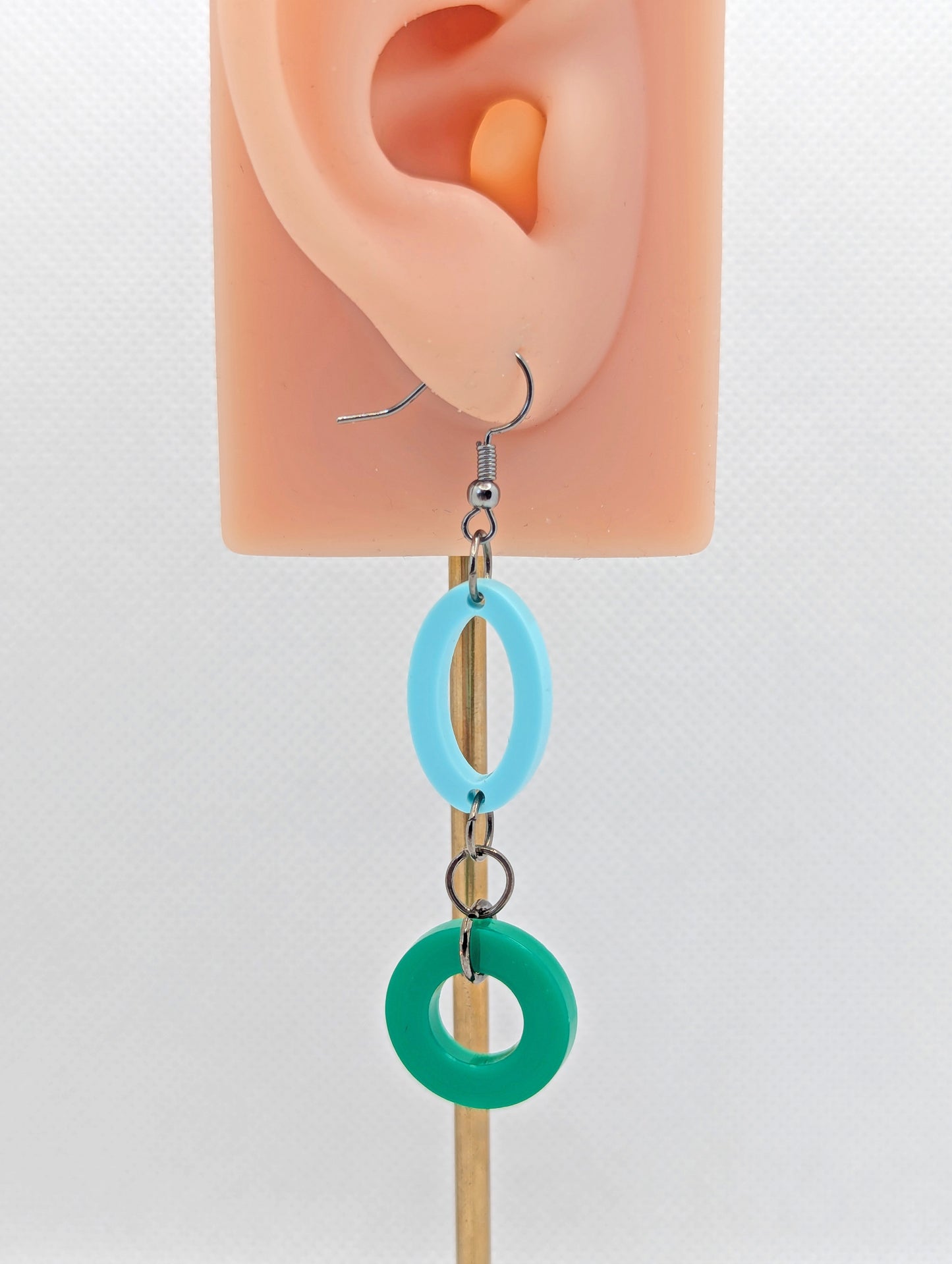 A two part drop earring with a Black ear wire hook fixing. It is  an oval with a circle dangling underneath joined by three Black jump rings. The colours are Spearmint for the oval and Green for the circle. it is on an ear to show the size.