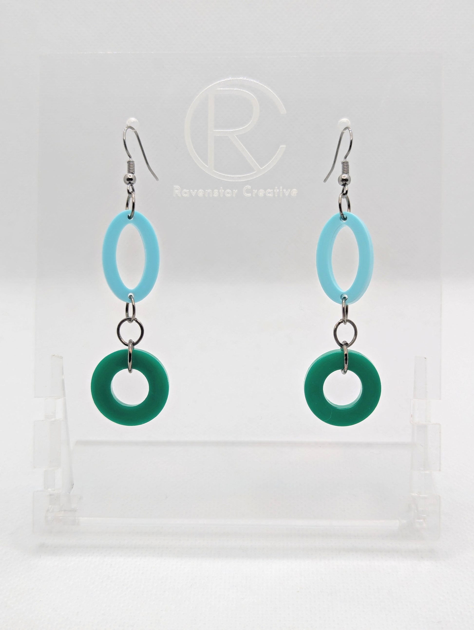 A pair of two part drop earrings with Black ear wire hook fixings. They are an oval with a circle dangling underneath joined by three Black jump rings. The colours are Spearmint for the oval and Green for the circle.