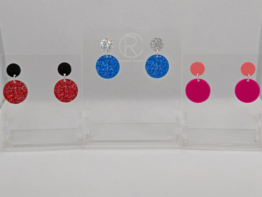 An image of three pairs of stud earrings, They are two circles with a larger one dangling underneath. The colours are Black and Red Glitter. Silver and Royal Blue Glitter, Sherbet Pin and Hot Pink.