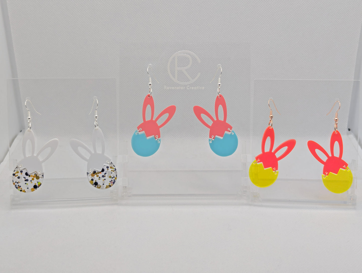 Three pairs of Drop earrings in two parts. The top part are bunny ears and the bottom is a broken egg. The colours are White ears and Lollipop Glitter for the egg. Sherbet Pink ears and Spearmint egg, Neon Pink ears and Neon Orange Egg.