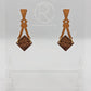 Image of a pair of wooden earrings. The design is a thin elegant top that forks out to support a diamond shape dangling under it. They are Cherry Wood for the top and a Walnut Wood diamond. They are against a white background on a clear stand.