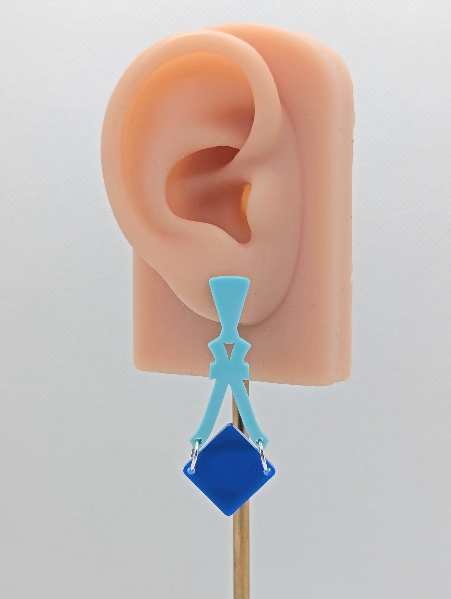 Image of a pair of acrylic earrings. The design is a thin elegant top that forks out to support a diamond shape dangling under it. They are Spearmint for the top and a Blue diamond. They are on an ear to show the size.