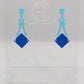 Image of a pair of acrylic earrings. The design is a thin elegant top that forks out to support a diamond shape dangling under it. They are Spearmint for the top and a Blue diamond. They are against a white background on a clear stand.