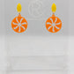 A pair of acrylic stud earrings. They are a small diamond shape with a spiral cut out of a circle dangling underneath. The colours are Yellow and Orange. They are on a clear stand with the Ravenstor Creative Logo against a white background.