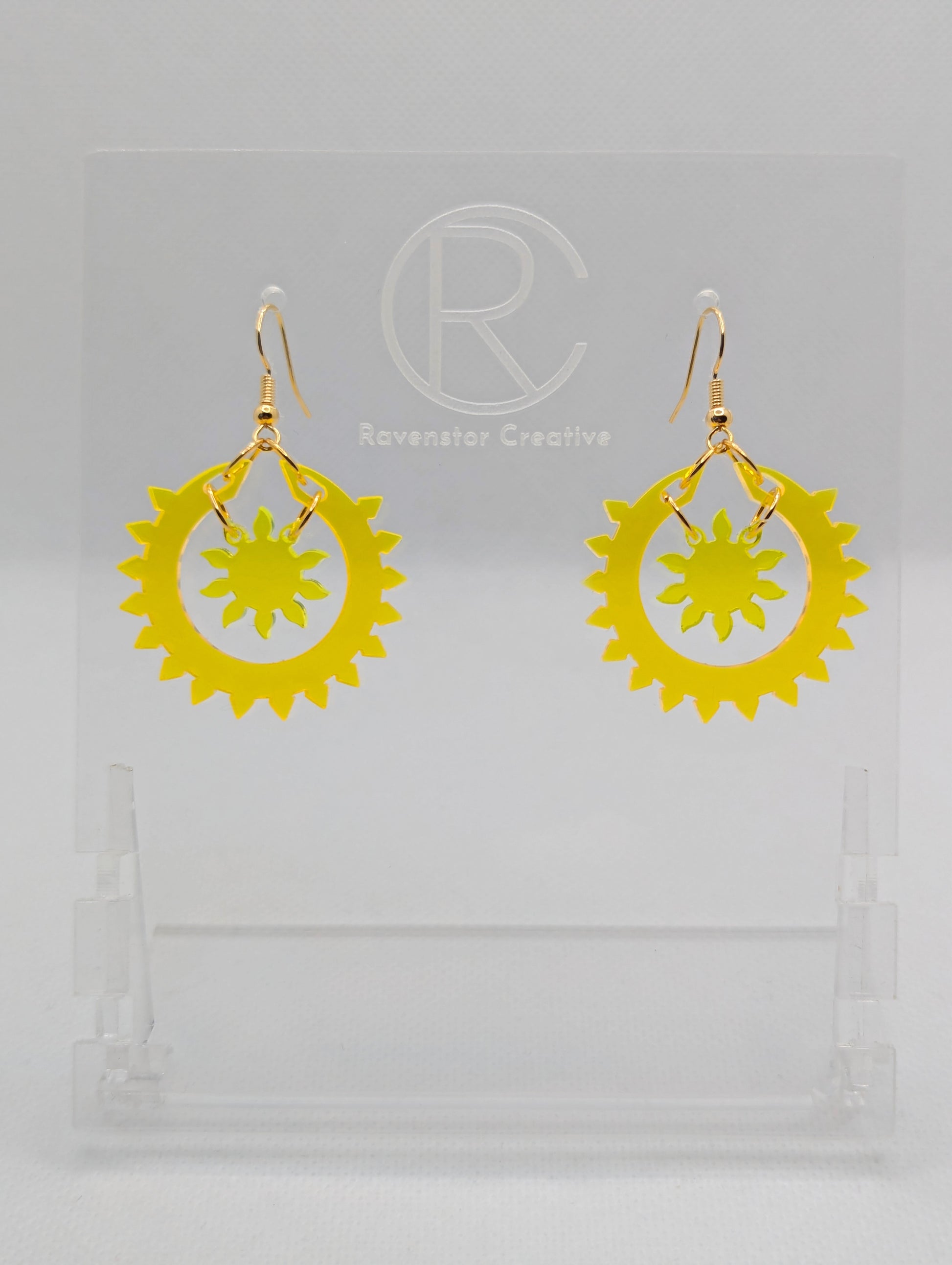 An image of a pair of drop earrings with Gold ear wire hook fixings, each in two parts. The outer circle has points around it with a small sun shape in the middle. The colours are Neon orange for the outer ring and Neon Yellow for the sun.