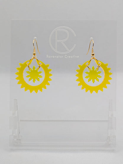 An image of a pair of drop earrings with Gold ear wire hook fixings, each in two parts. The outer circle has points around it with a small sun shape in the middle. The colours are Neon orange for the outer ring and Neon Yellow for the sun.