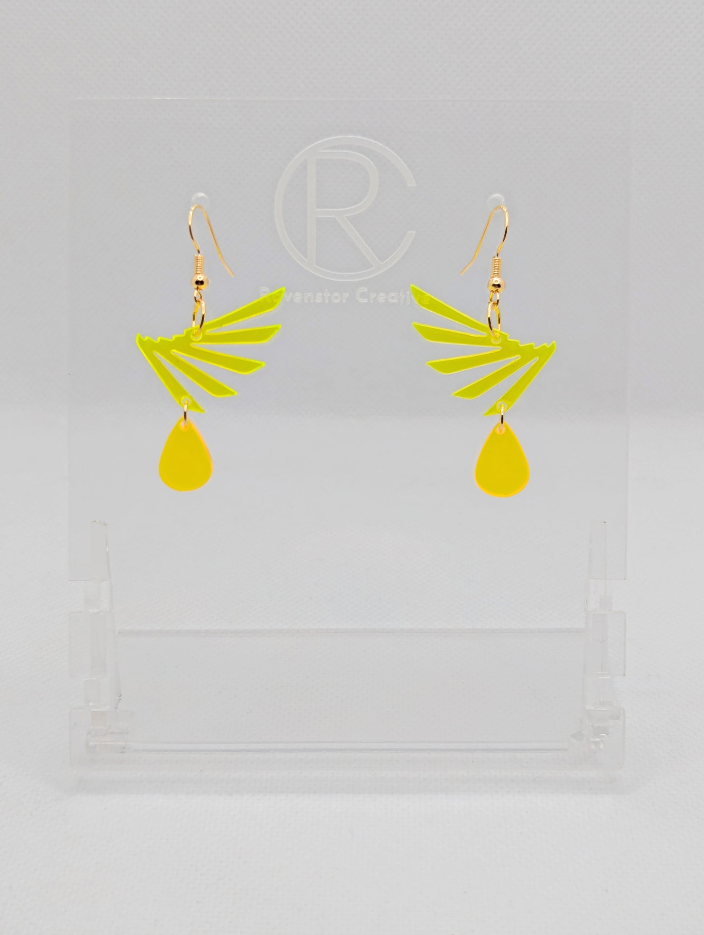 A pair of two part drop earrings with Gold ear wire hook fixings. Each one is a single wing with a teardrop balancing underneath it. The colours are Neon Yellow for the wing and neon orange for the teardrop. They are on clear stands.