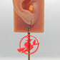 An earring on an ear to show the size with black silver ear wire fixings, they are a circle with a scene cut out of a witch on her broom with a cat perched on the broom. It is made from neon pink acrylic against a white background.